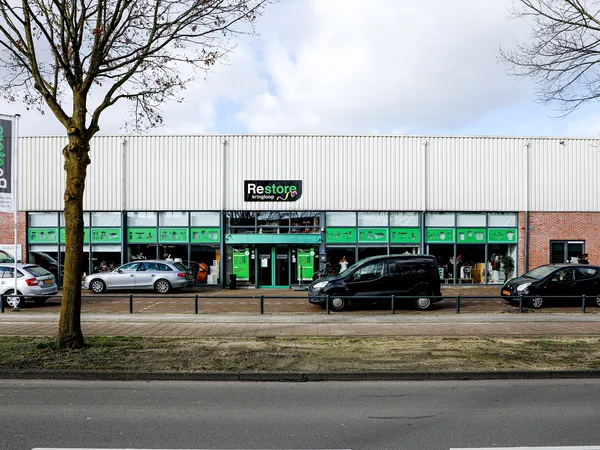 Groene gevel van Restore kringloopwinkel aan Groeneveldselaan met parkeerplaatsen ervoor