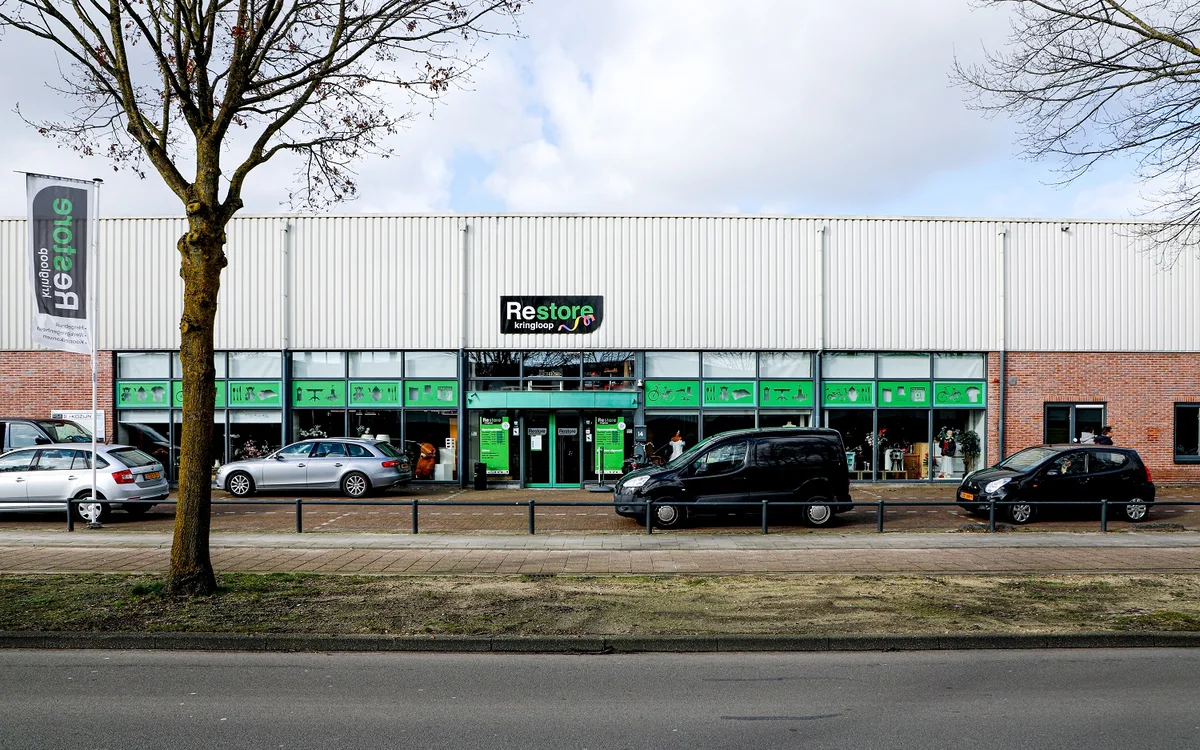 Groene gevel van Restore kringloopwinkel aan Groeneveldselaan met parkeerplaatsen ervoor