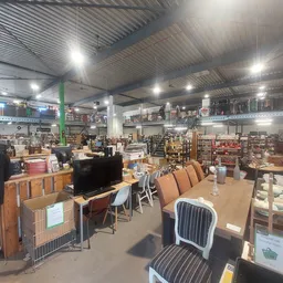 Overzicht van kringloopwinkel met meubels, stoelen, televisie en diverse spullen op de vloer en stellingen