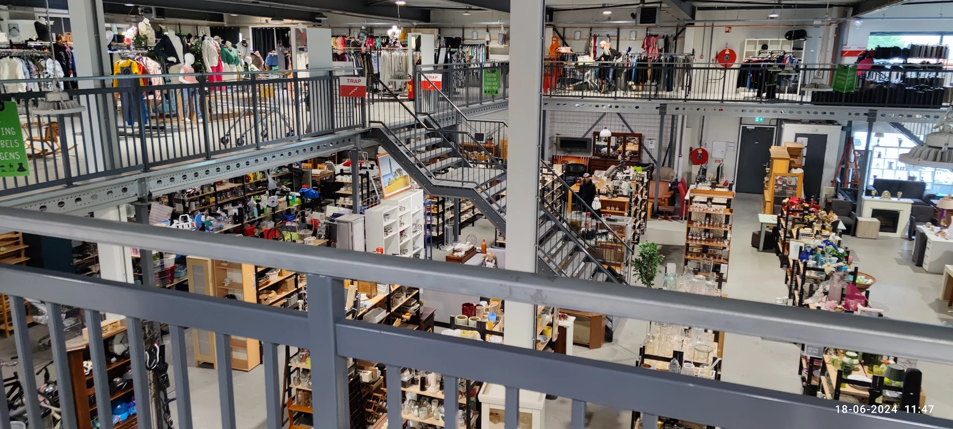 Meerdere verdiepingen van een kringloopwinkel met trappen, stellingen en diverse tweedehandsartikelen
