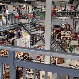 Meerdere verdiepingen van een kringloopwinkel met trappen, stellingen en diverse tweedehandsartikelen