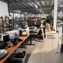 Winkelvloer met houten tafels, stellingen met diverse spullen, planten en huisraad in een kringloopwinkel