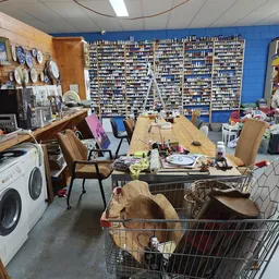 Winkelvloer met werkplekken, wasmachines, blauw muurrek met veel artikelen, winkelwagen en diverse spullen
