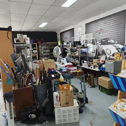 Volle werkplaats of magazijn met gereedschap, onderdelen en diverse spullen op stellingen en tafels