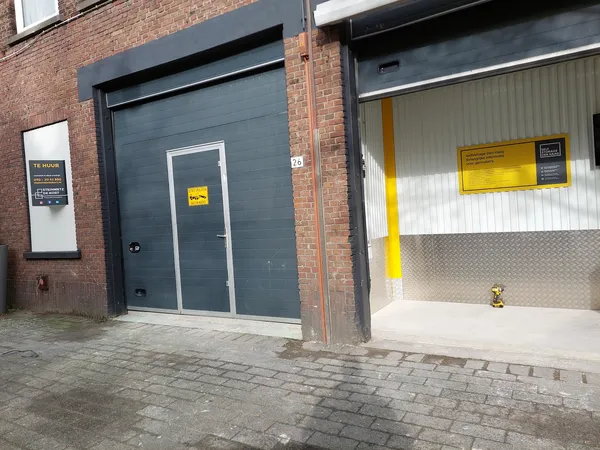 Grijze garagedeur en witte metalen deur met gele waarschuwingsstickers op bakstenen gevel
