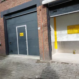 Grijze garagedeur en witte metalen deur met gele waarschuwingsstickers op bakstenen gevel