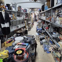 Winkelpad tussen stellingen vol huishoudelijke artikelen, servies, kookgerei en diverse spullen in een kringloopwinkel