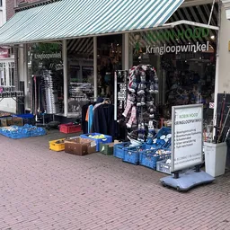 Voorkant van kringloopwinkel met uitgestalde kleding, dozen en spullen op straat