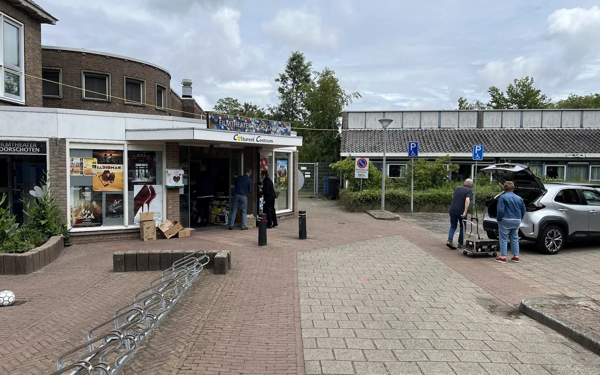 Voorgevel van kringloopwinkel met etalage, ingang en parkeerplaats met auto's en bezoekers