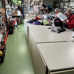 Winkelvloer met grote werktafels waarop diverse kleding en textiel uitgestald ligt, medewerkers sorteren spullen