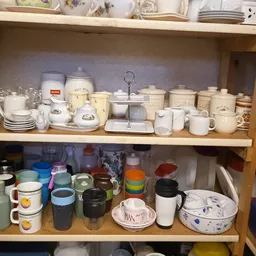 Twee schappen vol wit serviesgoed, bekers, kannen en huishoudelijke artikelen