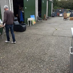 Binnenplein van kringloopwinkel met betonnen vloer, diverse meubels en spullen op achtergrond