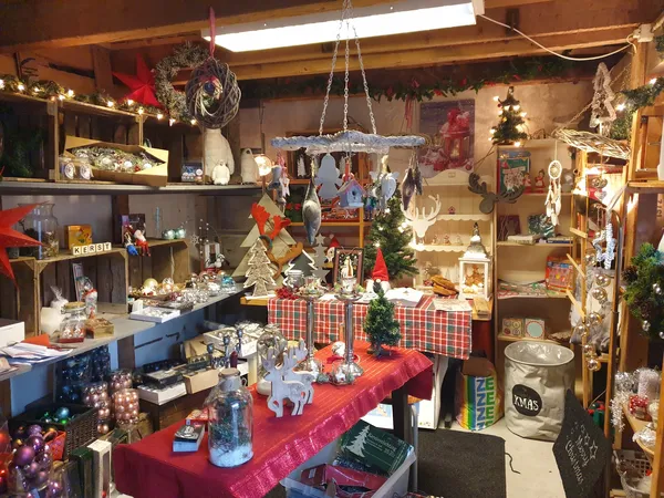 Kringloopwinkel met kerstversiering, rode tafels met diverse spullen, hangende decoraties en verlichte stellingen