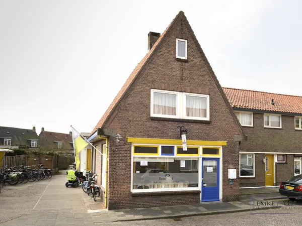 Bakstenen gevel van kringloopwinkel met gele en blauwe pui, etalageruit en ingangseur aan straat
