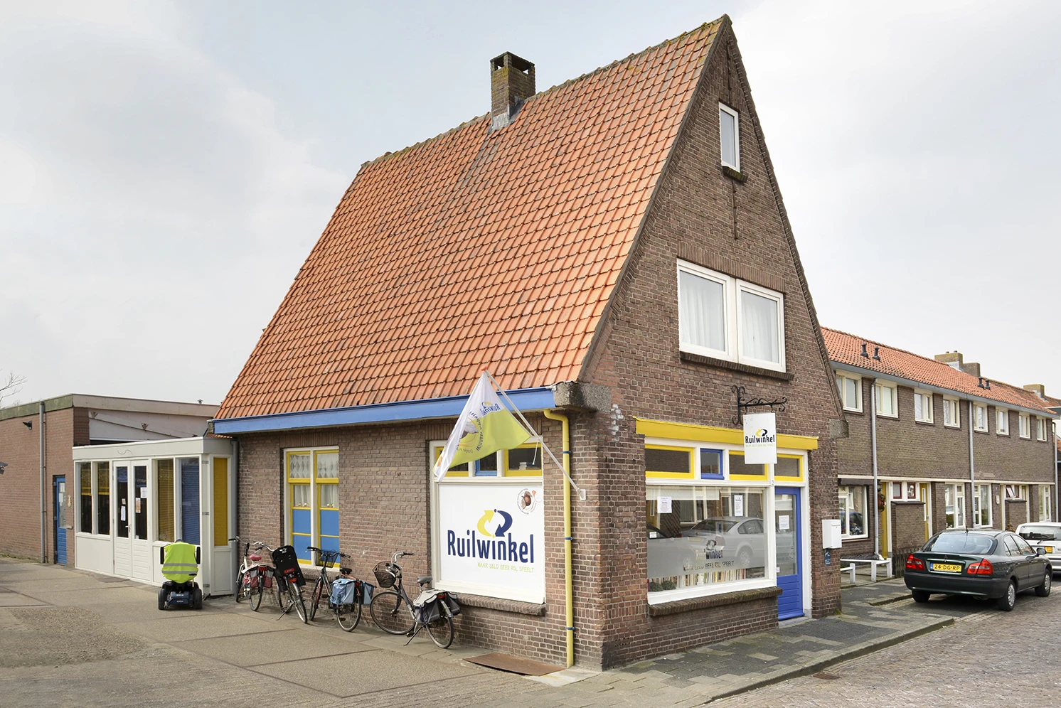 Voorgevel van Ruilwinkel Goes, een bakstenen pand met rood pannendak, winkelpui met blauw accenten en de winkelnaambord zicht