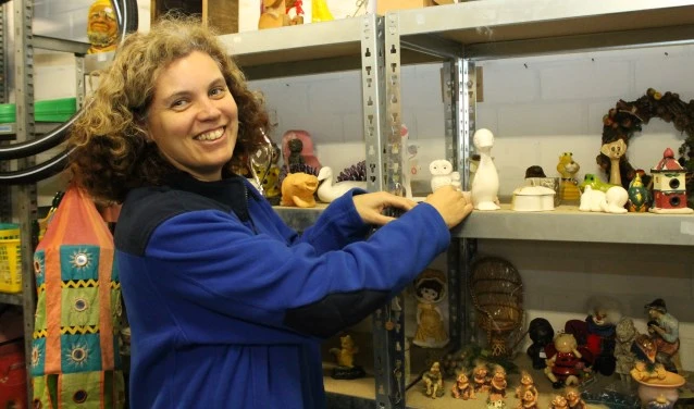 Medewerker wijst naar collectie poppen en speelgoed in stellingen van de kringloopwinkel