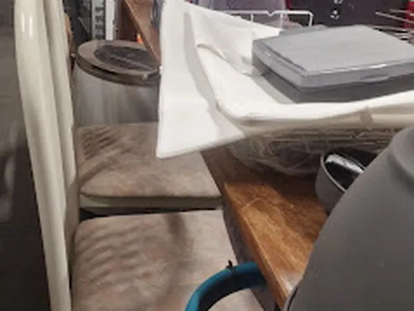 Zicht op kringloopwinkelinterieur met houten tafel, witte divider en diverse spullen op achtergrond