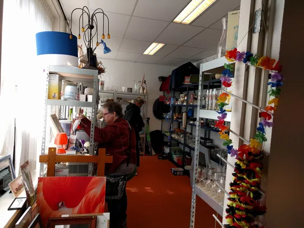 Interieur van kringloopwinkel met stellingen vol spullen, een medewerker achter in de winkel, en kleurrijke decoratie aan de 
