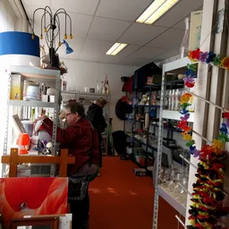 Interieur van kringloopwinkel met stellingen vol spullen, een medewerker achter in de winkel, en kleurrijke decoratie aan de 