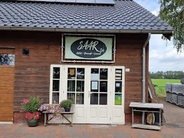 Voorgevel van kringloopwinkel Saartje met houten gevel, witte deuren, logo bord en bloempotten