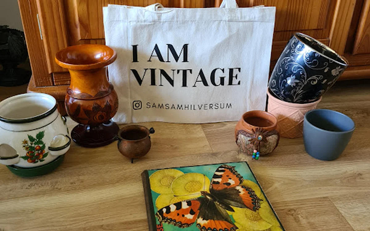 Vintage items op houten tafel: keramische potten, kandelaar, borden en decoratief boek met vlinders