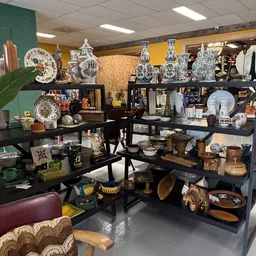 Uitgestalde decoratieve artikelen: porselein borden, vazen, schalen en houten voorwerpen op zwarte kasten en stellingen