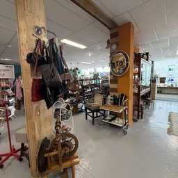 Winkelvloer met houten zuil, uitgestalde tassen, spiegels, stoelen en diverse inboedel in een kringloopwinkel