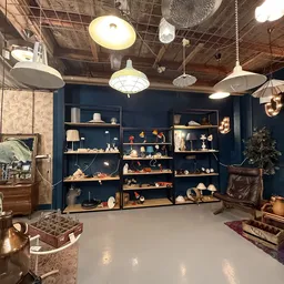 Uitgestalde tweedehands huishoudartikelen en decoratie op houten stellingen tegen donkerblauwe muur