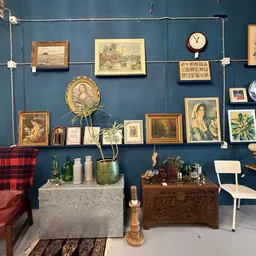Wand met uitgestalde vintage schilderijen, portretten, klokken en decoratieve items boven twee kasten met vazen en plantjes