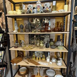 Vitrinekast met antieke en decoratieve items zoals beelden, serviesgoed, kandelaars en diverse kunstobjecten