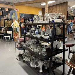 Zwarte stellingen volgestapeld met glaswerk, servies en huishoudelijke artikelen in de kringloopwinkel