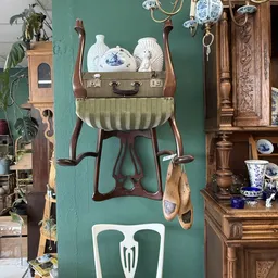 Vintage interieurstukken: bruine houten stoel met groene zitting, bruine vintage koffer, witte porseleinen vazen en houten ob