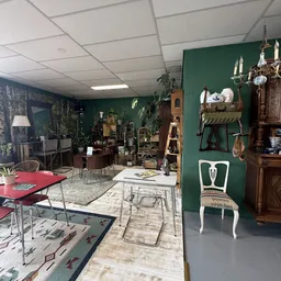 Winkelvloer met groene muur, vintage meubels, tafels met stoelen en diverse tweedehands spullen