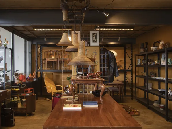 Winkelvloer van kringloopwinkel met houten toonbank, hanglampen, stellingen met spullen en diverse meubels