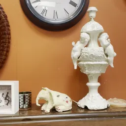 Witte decoratieve porseleinen urn met handvaten en vogelornament naast een witte porseleine olifantbeeldje