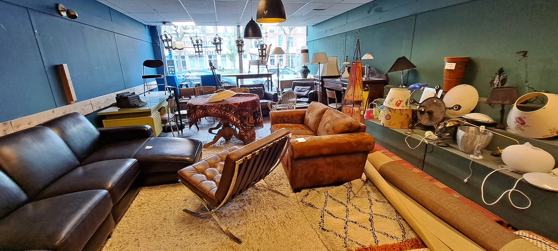 Ruim interieur van kringloopwinkel met diverse meubels: lederen stoelen, zitbanken, tafels, hangende lampen en decoratie