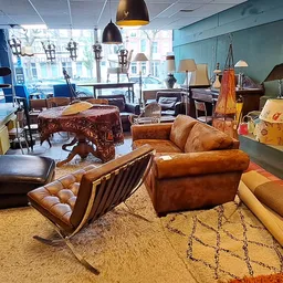 Ruim interieur van kringloopwinkel met diverse meubels: lederen stoelen, zitbanken, tafels, hangende lampen en decoratie