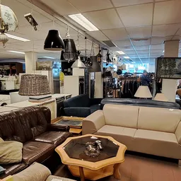 Winkelvloer met bruine leren bank, crèmekleurige zitbank en houten salontafel, achter winkelrekken met kleding en hangende ar