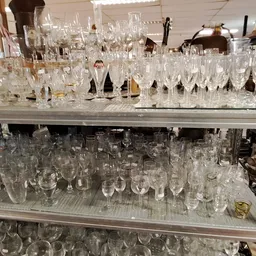 Glazen servies en drinkglazen uitgestald op metalen stellingen in een kringloopwinkel