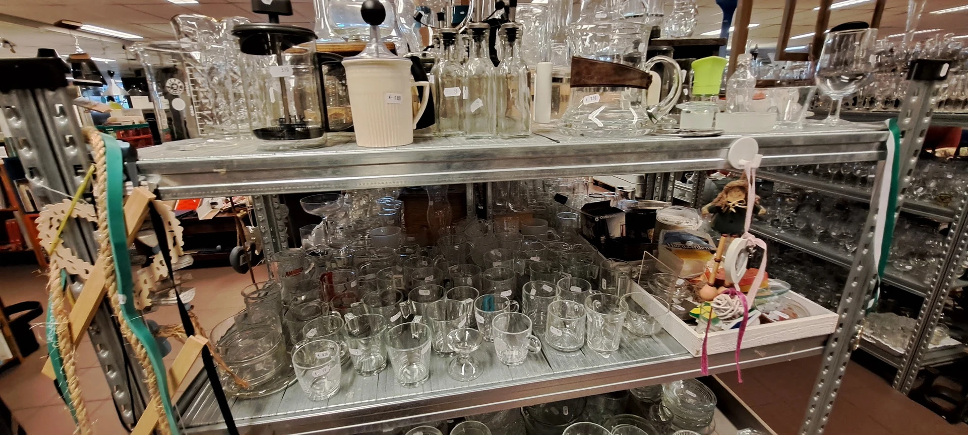 Glazen en drinkglazen uitgestald op planken in de kringloopwinkel