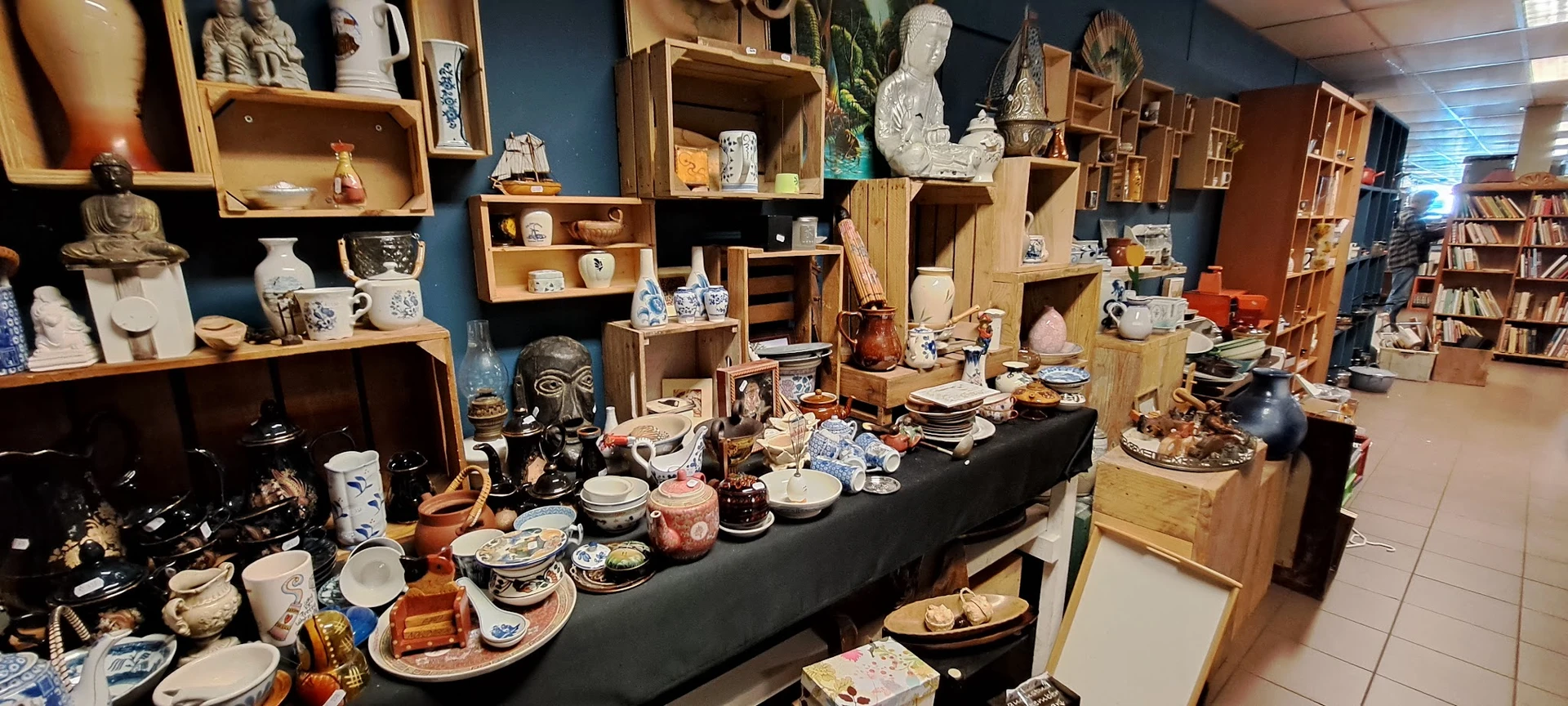Uitgestalde serviesgoed, decoratieve items en huishoudartikelen op tafel en in houten stellingen