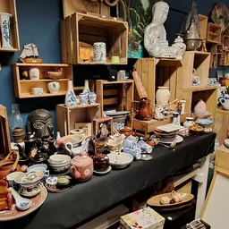 Uitgestalde serviesgoed, decoratieve items en huishoudartikelen op tafel en in houten stellingen