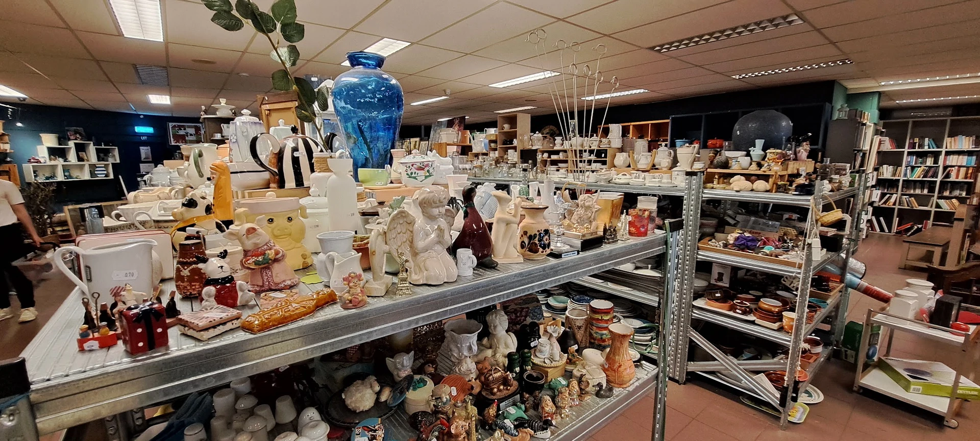 Stellingen en toonbank volgestapeld met diverse huishoudelijke artikelen, vazen, beelden en decoratieve voorwerpen in een kri