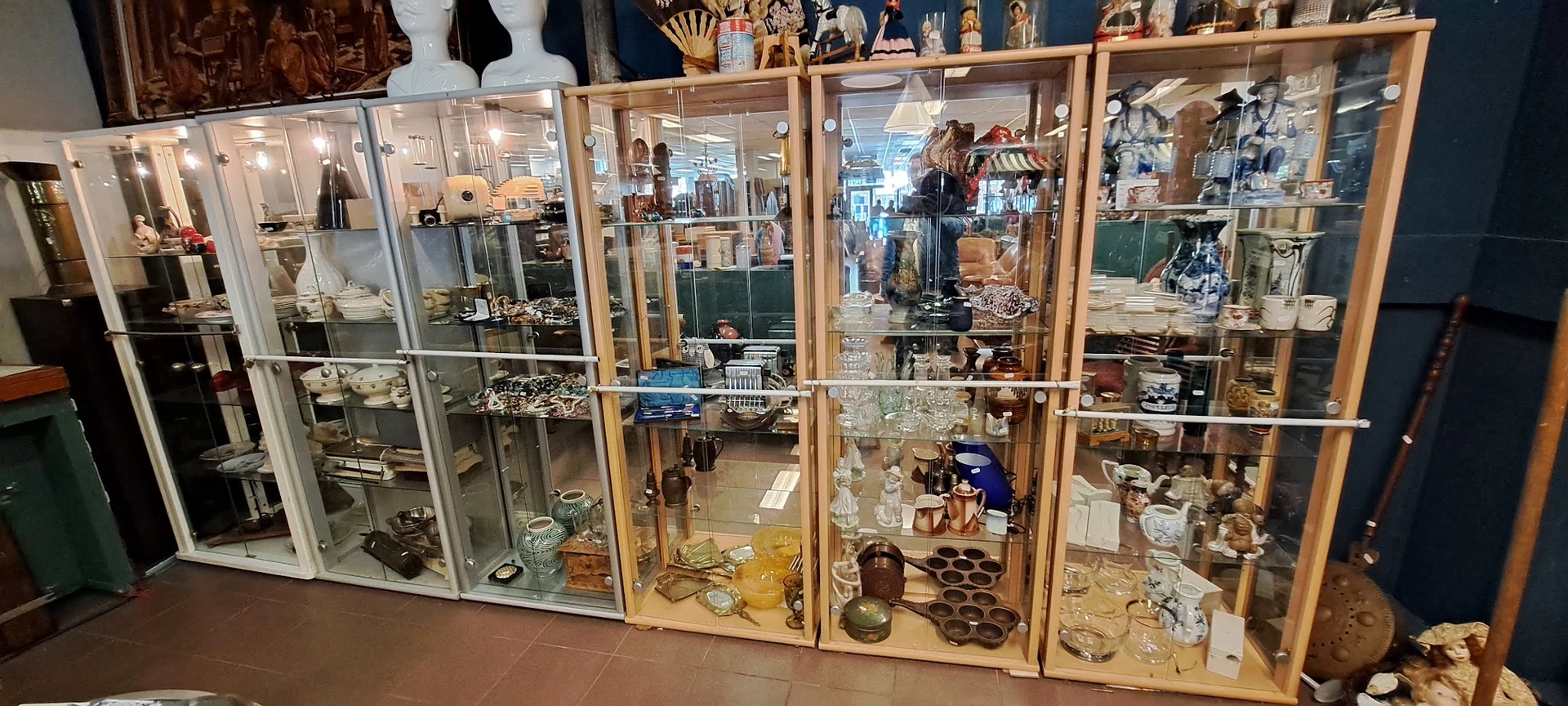 Vitrinekasten met diverse glazen, servies, decoratieve items en huishoudartikelen in een kringloopwinkel
