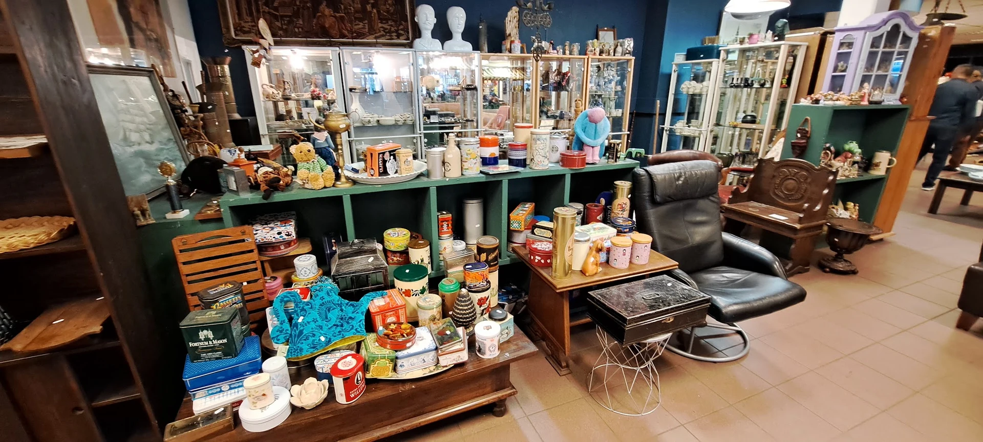 Uitgestalde huishoudelijke artikelen, servies, tinnen en decoratie op tafels en in groene stellingkast