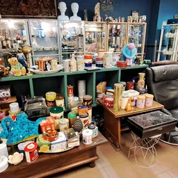 Uitgestalde huishoudelijke artikelen, servies, tinnen en decoratie op tafels en in groene stellingkast