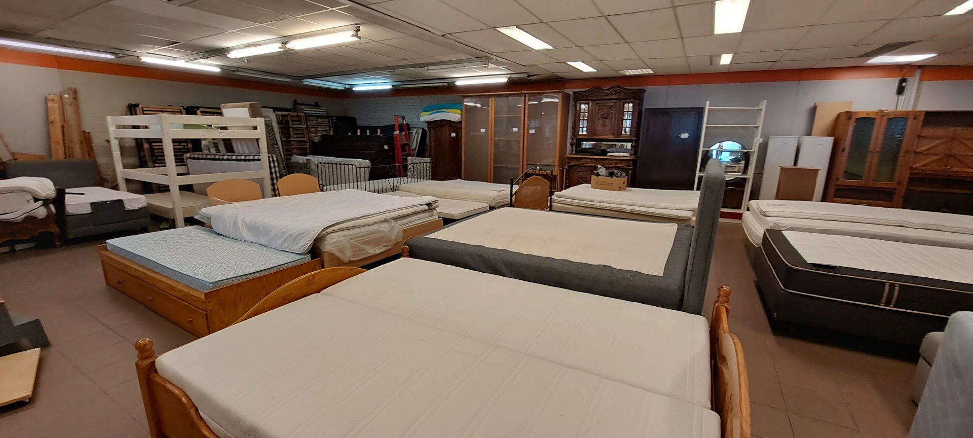 Uitgestalde bedden en matrassen in de winkel, waaronder houten en grijze bedframes met witte matrassen