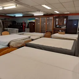 Uitgestalde bedden en matrassen in de winkel, waaronder houten en grijze bedframes met witte matrassen