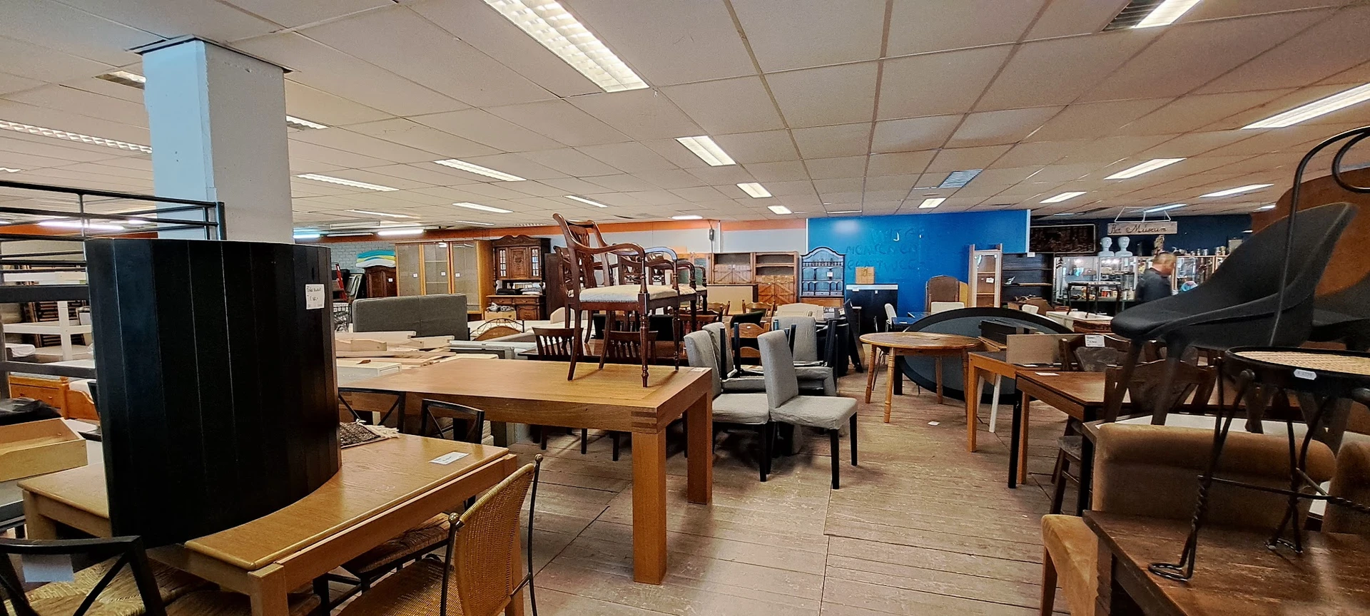 Winkelvloer met diverse meubels: houten tafels, stoelen, kasten en andere meubelstukken uitgestald onder fluorescente verlich