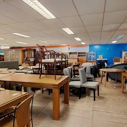 Winkelvloer met diverse meubels: houten tafels, stoelen, kasten en andere meubelstukken uitgestald onder fluorescente verlich
